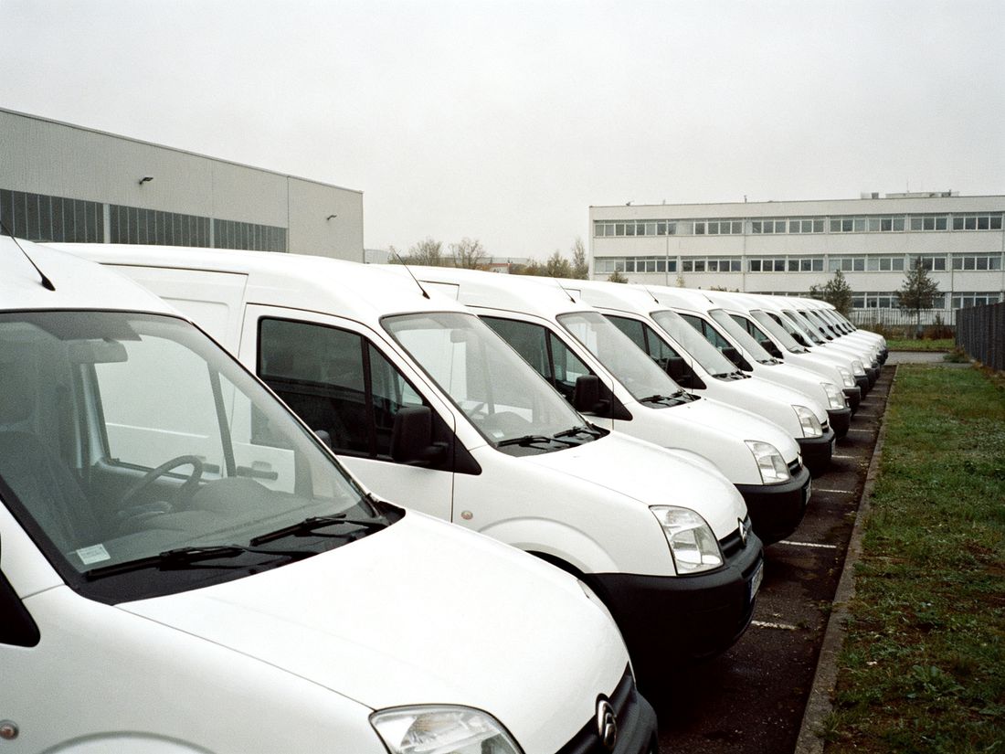 Reihe weißer Transporter ohne Beschriftung auf einem Firmenhof